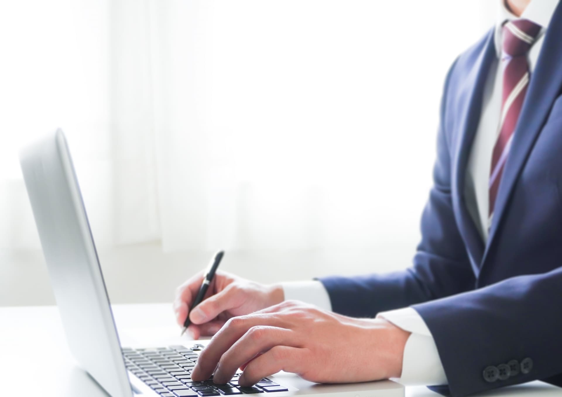 パソコンを打ちながら、何かを書くビジネスマン